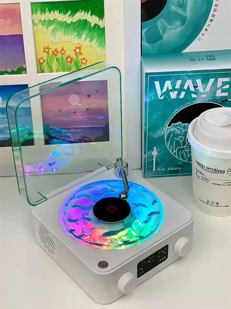 Small turntable with colorful LED lights on a white surface, surrounded by framed pictures and a container.