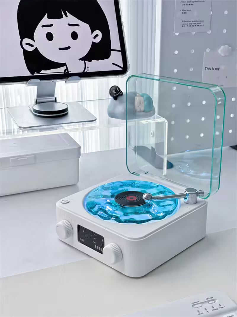 Modern turntable with a glass cover on a desk, with a computer monitor in the background.