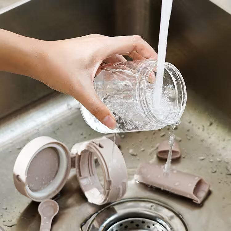 Person washing a glass jar over a sink with kitchen utensils nearby