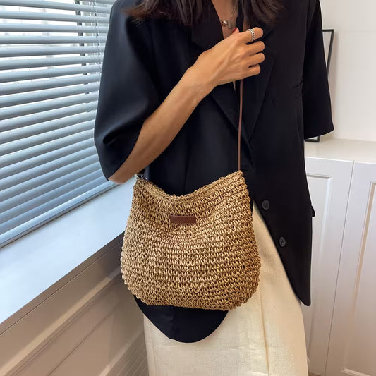Person holding a woven handbag in a room with a window and white cabinets.
