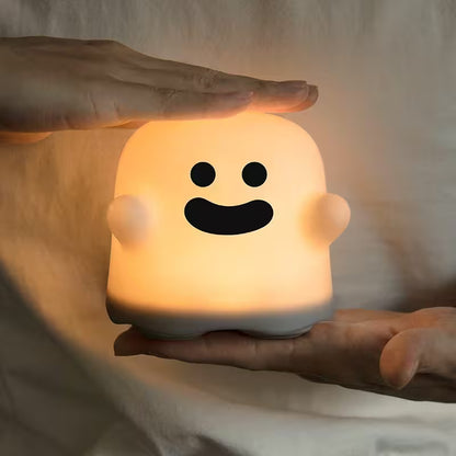 Cute ghost-shaped night light held by a hand on a soft beige background