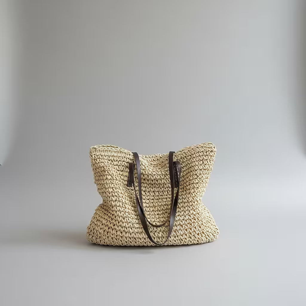 Woven straw bag with leather handles on a light gray background