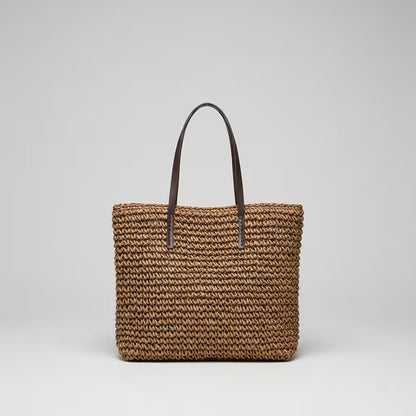 Woven brown bag with a black handle on a light gray background