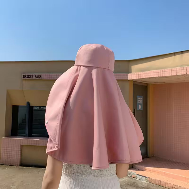 Person wearing a pink hooded coat standing in front of a building with a blue sky.