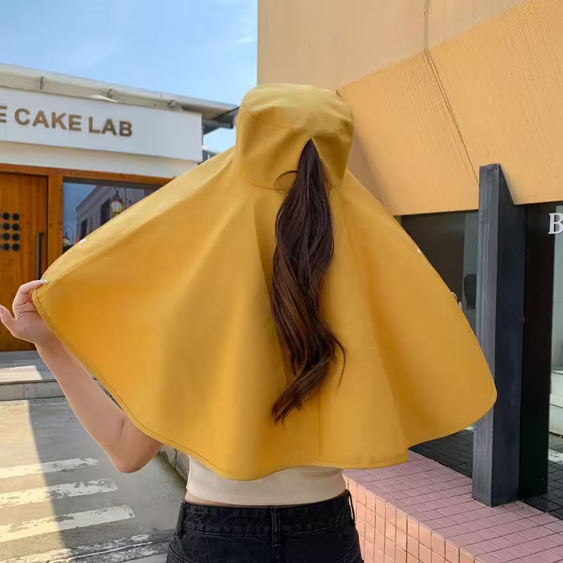 Person wearing a yellow raincoat with a ponytail, standing on a sidewalk.