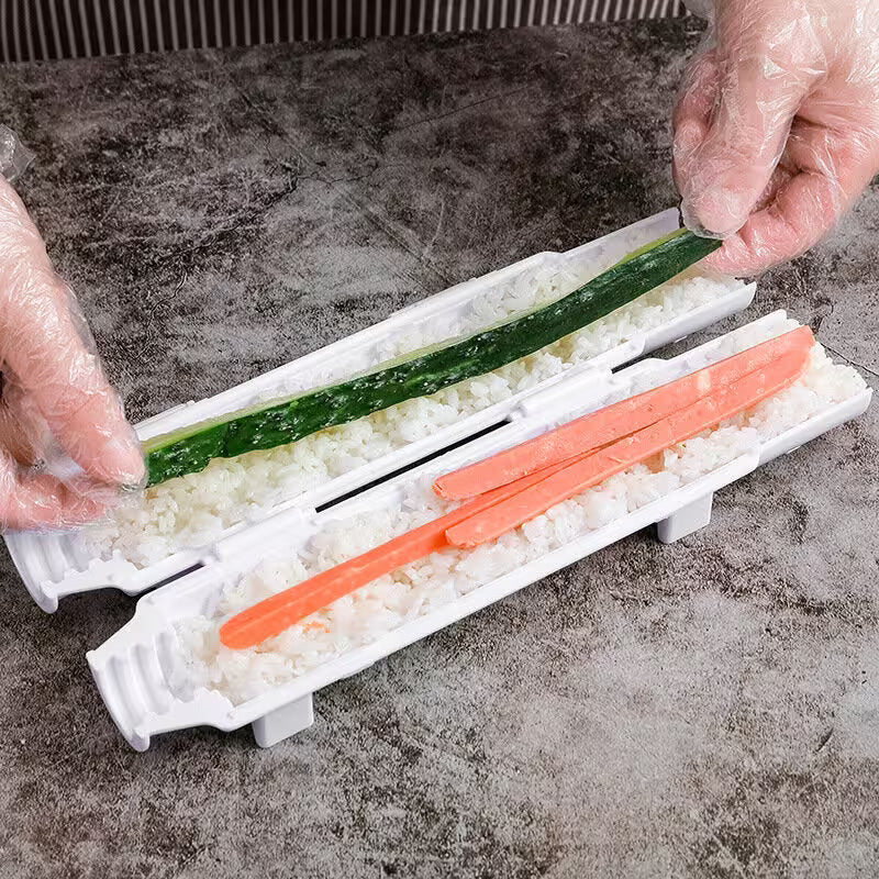 Hands preparing sushi with a rice mold and vegetable slices on a gray surface.