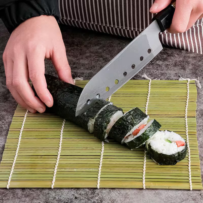 Person cutting sushi rolls with a knife on a bamboo mat
