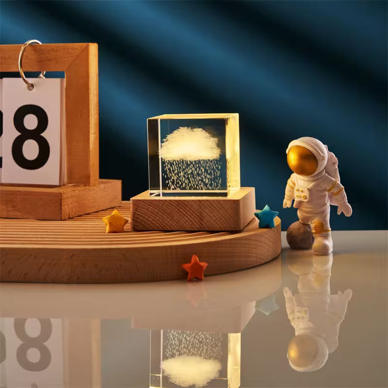 Decorative setup with a wooden frame, glass box with cloud design, and small astronaut figure on a reflective surface.