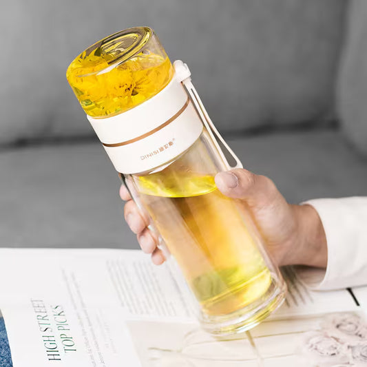 Hand holding a transparent water bottle with yellow liquid and a white lid, sitting on a surface with a magazine.