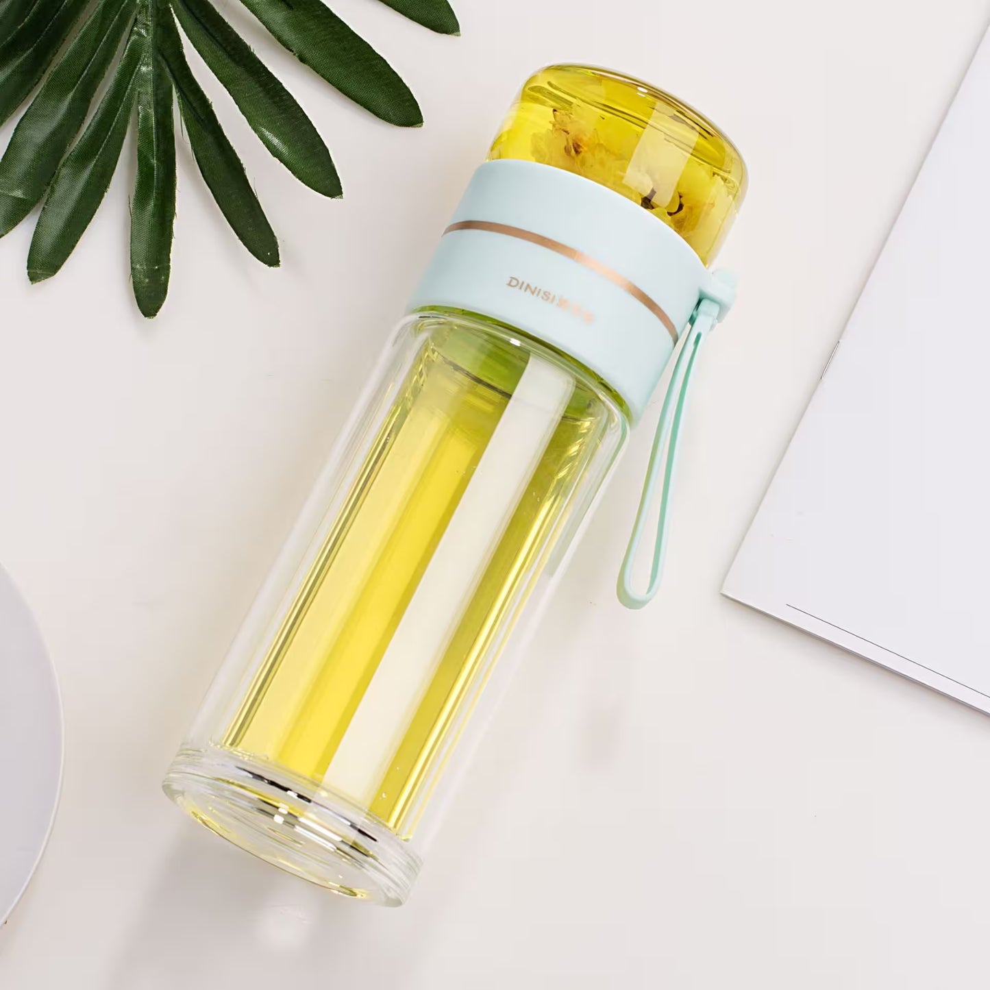 Clear water bottle with yellow liquid on a light surface with green leaves