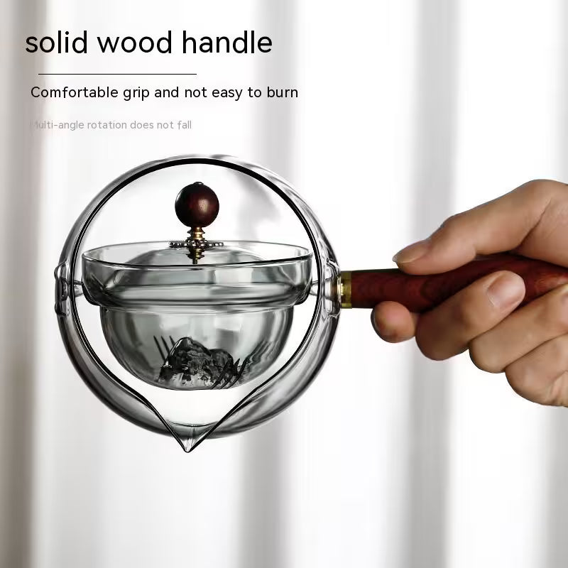 Glass tea infuser with a solid wood handle held by a hand on a white background