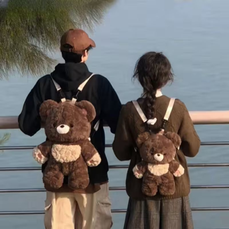 Two people wearing teddy bear backpacks by a body of water.