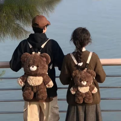 Two people wearing teddy bear backpacks by a body of water.
