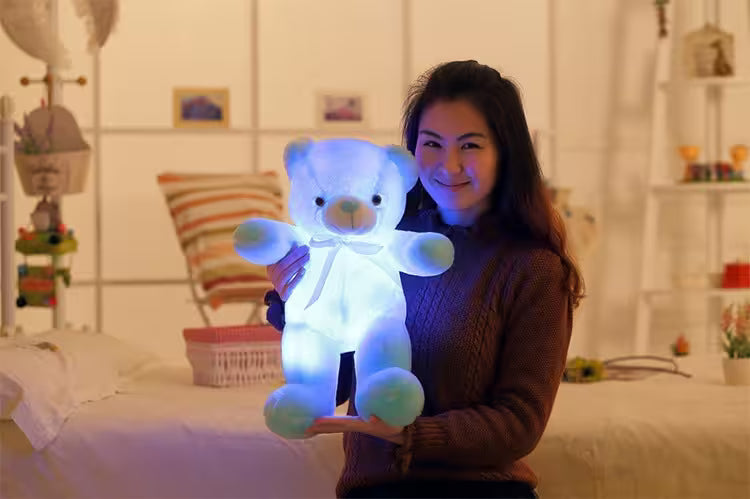 Woman holding a glowing teddy bear in a bedroom setting