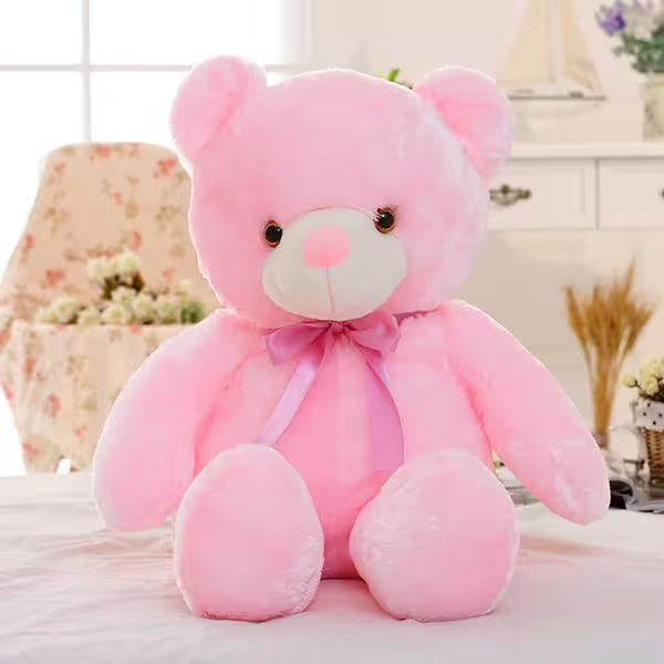 Large pink teddy bear with a bow tie on a soft surface.