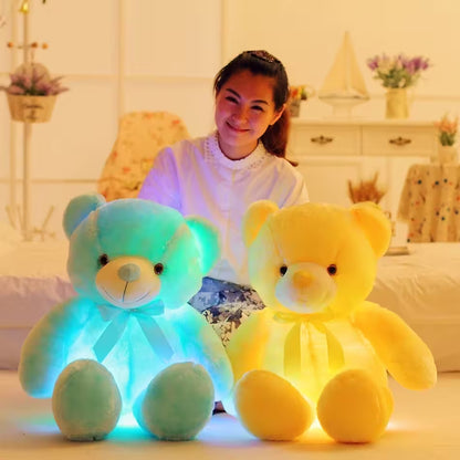 Two glowing teddy bears, one blue and one yellow, in a room with a person sitting behind them.