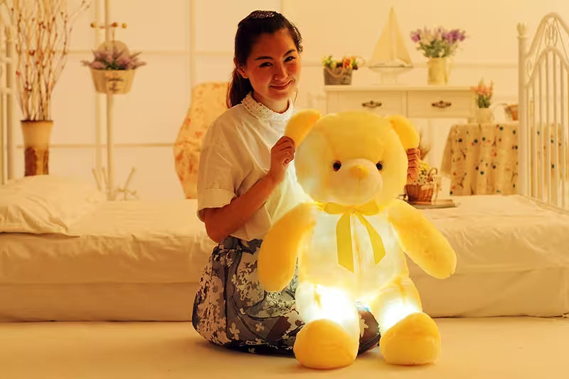 Woman holding a glowing yellow teddy bear in a bedroom setting