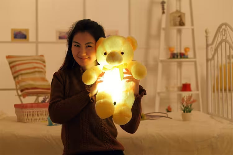 Person holding a glowing yellow teddy bear in a bedroom setting