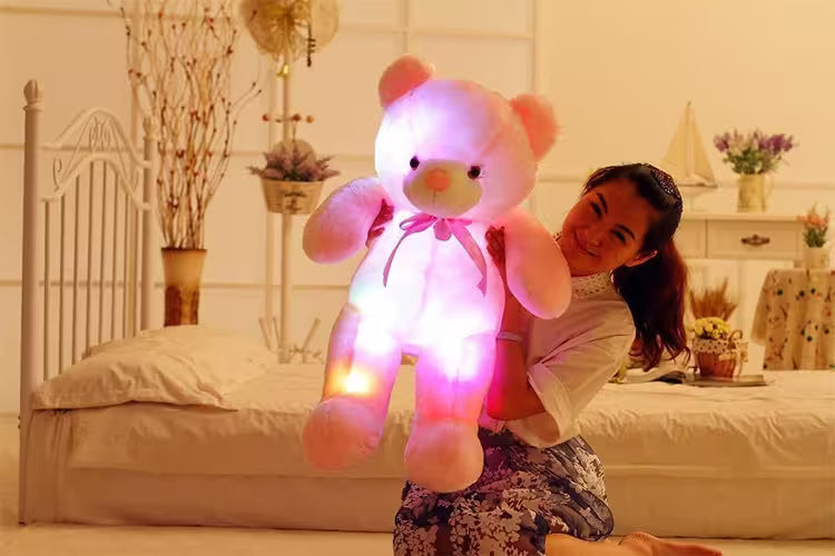 Person holding a large, glowing teddy bear in a bedroom setting
