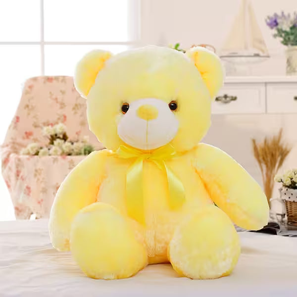 Yellow teddy bear plush toy on a light-colored surface with a blurred indoor background