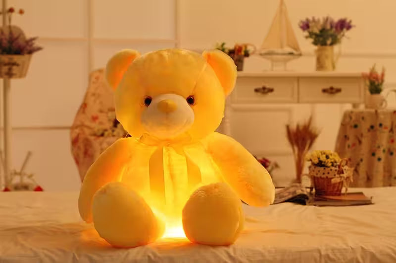 Yellow glowing teddy bear on a bed with a blurred room background