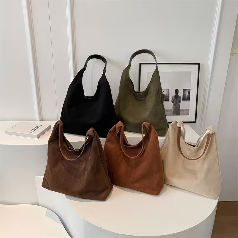 Five handbags in black, green, brown, and beige on a white surface with a minimal background.