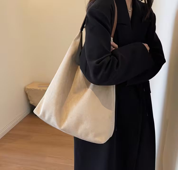 Person wearing a black coat holding a beige tote bag indoors.