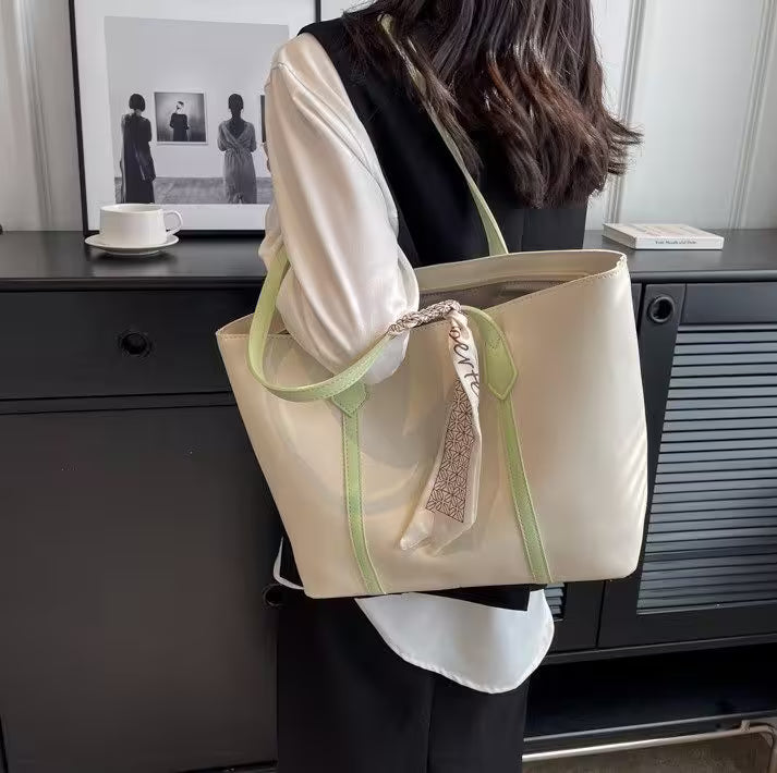 Person holding a beige tote bag with green straps in an indoor setting.