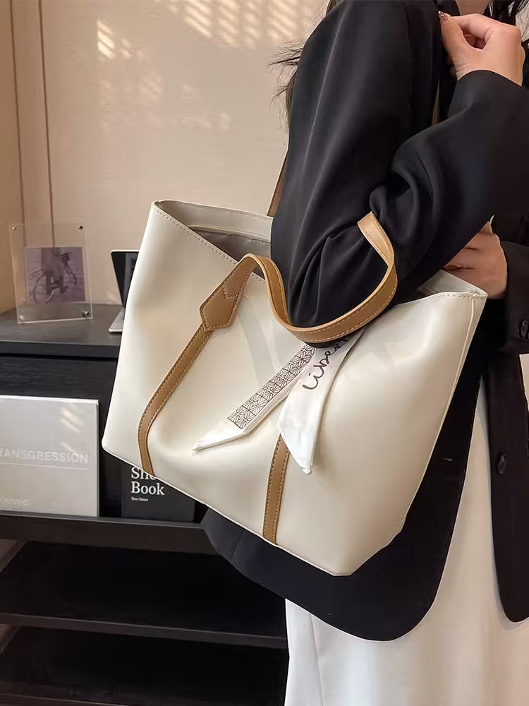 Person holding a white handbag with brown accents, wearing a black coat.