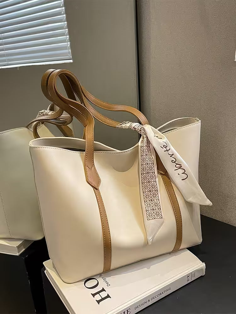 Beige handbag with brown handles on a stack of books, with a visible brand tag.