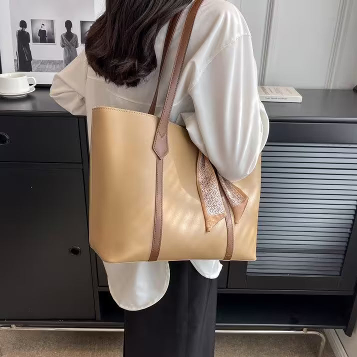 Person holding a beige tote bag with brown straps in an indoor setting.