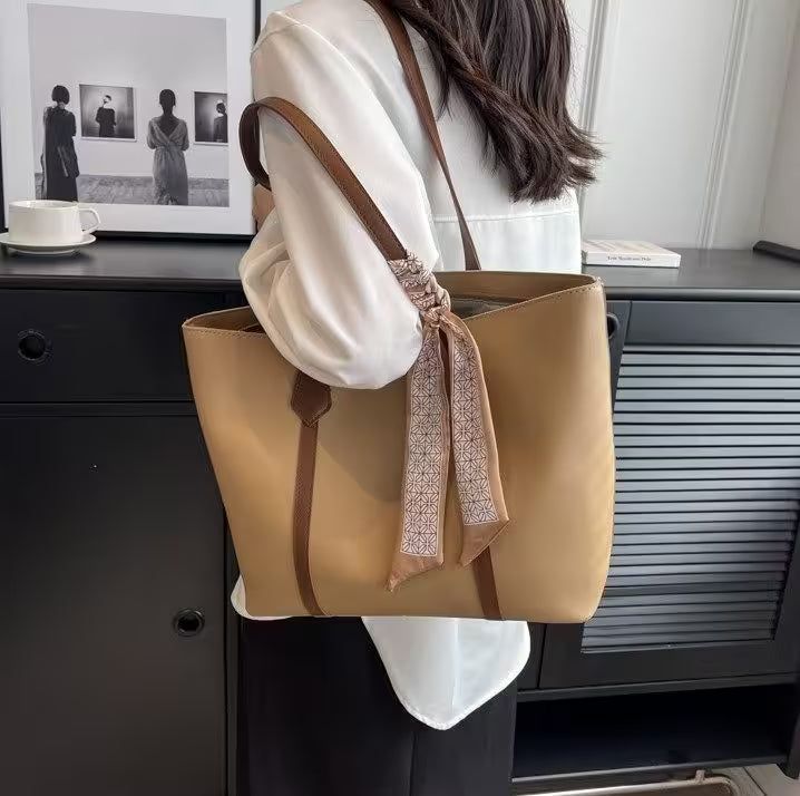 Person holding a beige tote bag with a brown strap in an indoor setting