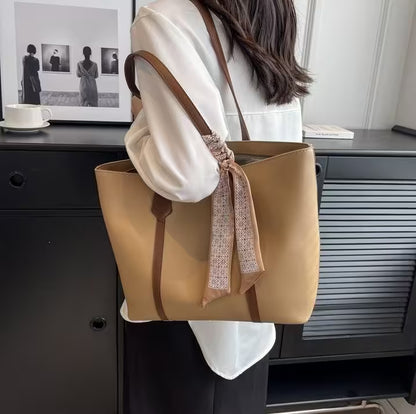 Person holding a beige tote bag with a brown strap in an indoor setting