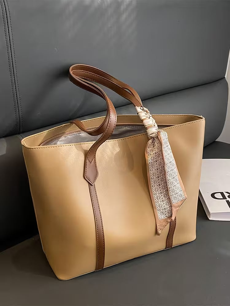 Beige tote bag with brown handles and a decorative ribbon on a gray surface.