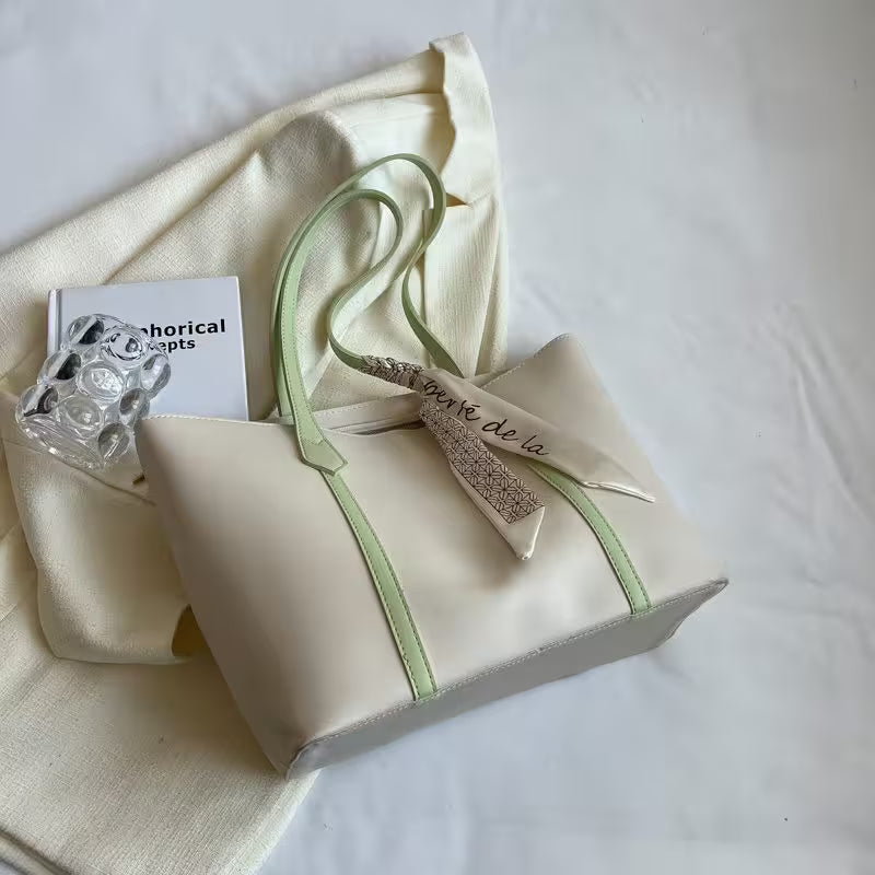 Beige tote bag with green strap and ribbon on a white surface