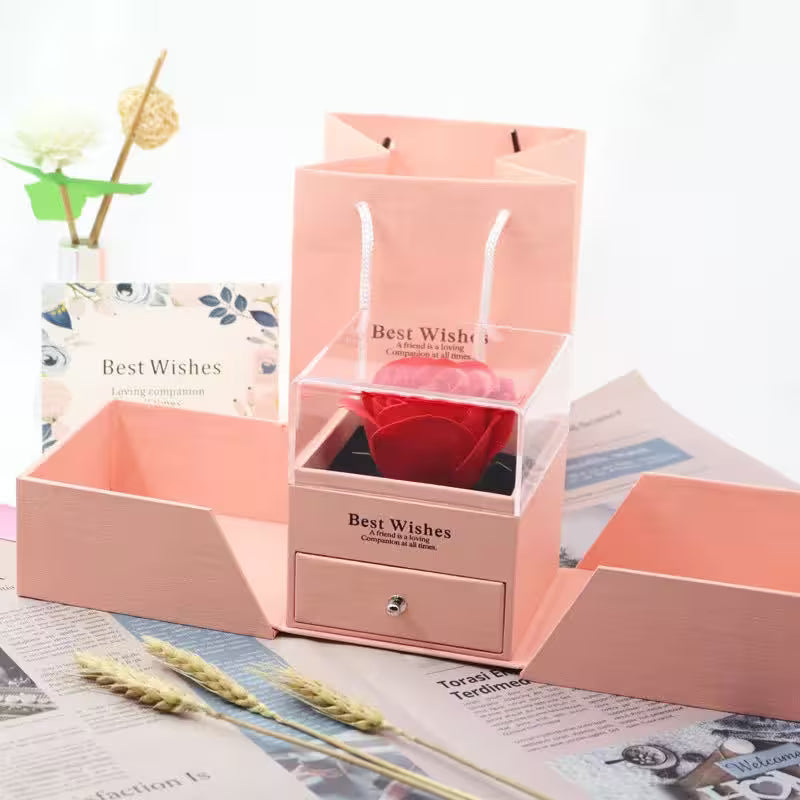 Pink jewelry box with clear top, 'Best Wishes' text, on a newspaper background