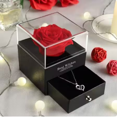 Black gift box with a red rose and heart-shaped necklace on a decorative surface.