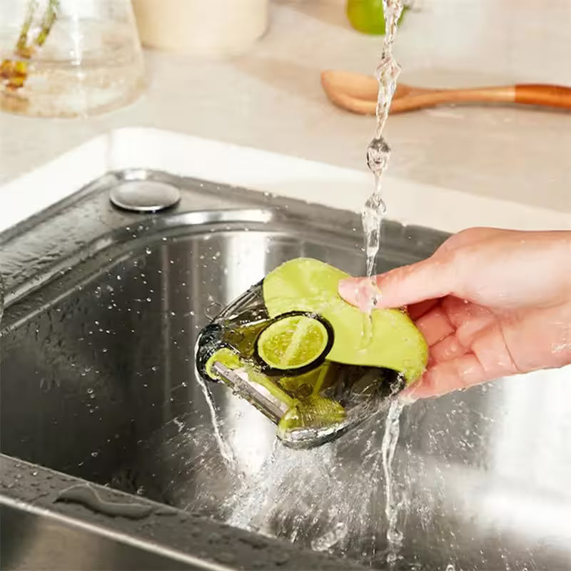 Person washing a green sponge in a kitchen sink with water running over it.