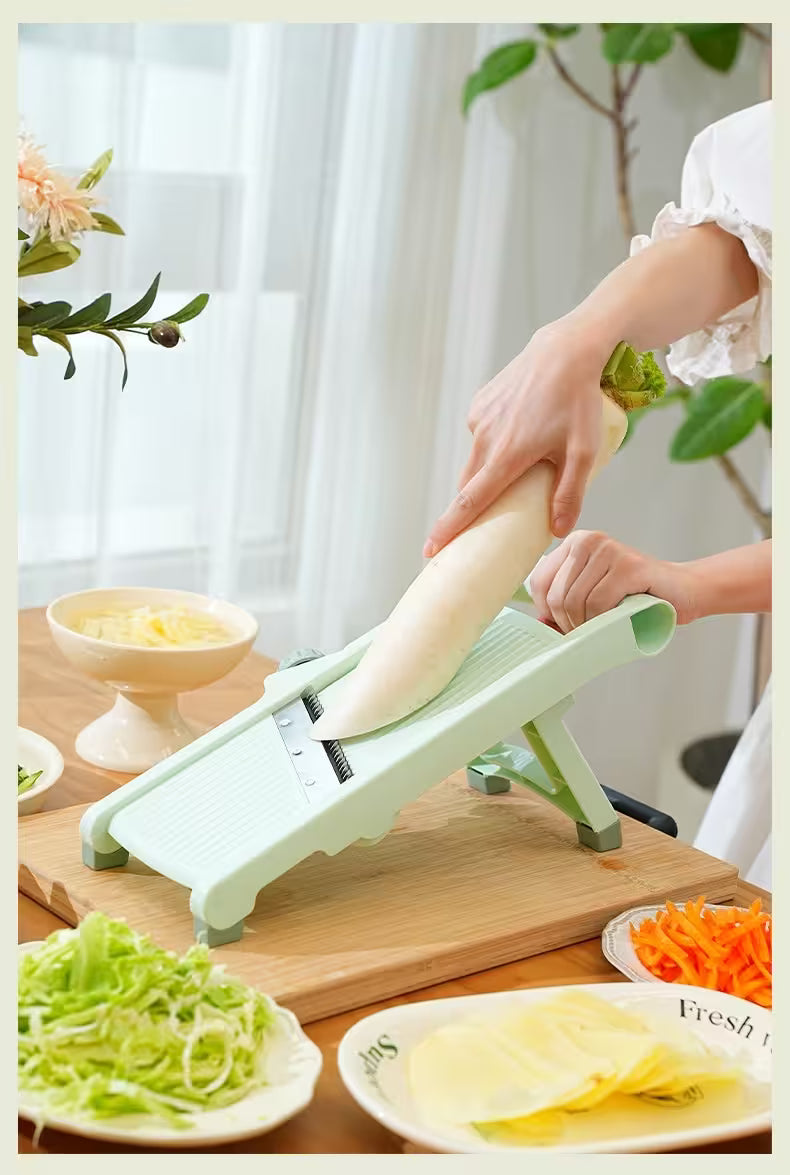 Person using a green mandoline slicer to slice vegetables on a wooden cutting board.