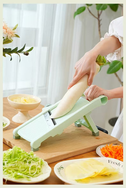 Person using a green mandoline slicer to slice vegetables on a wooden cutting board.