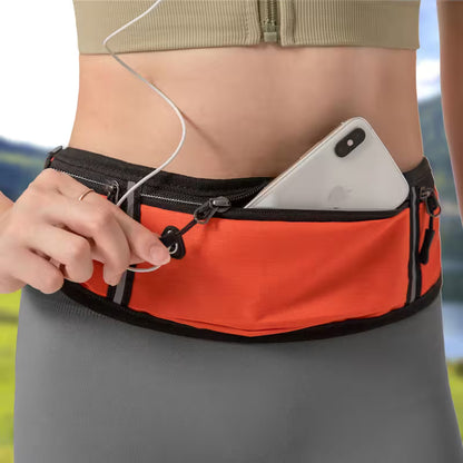 Person wearing an orange waist bag with a phone and earphones, outdoors.
