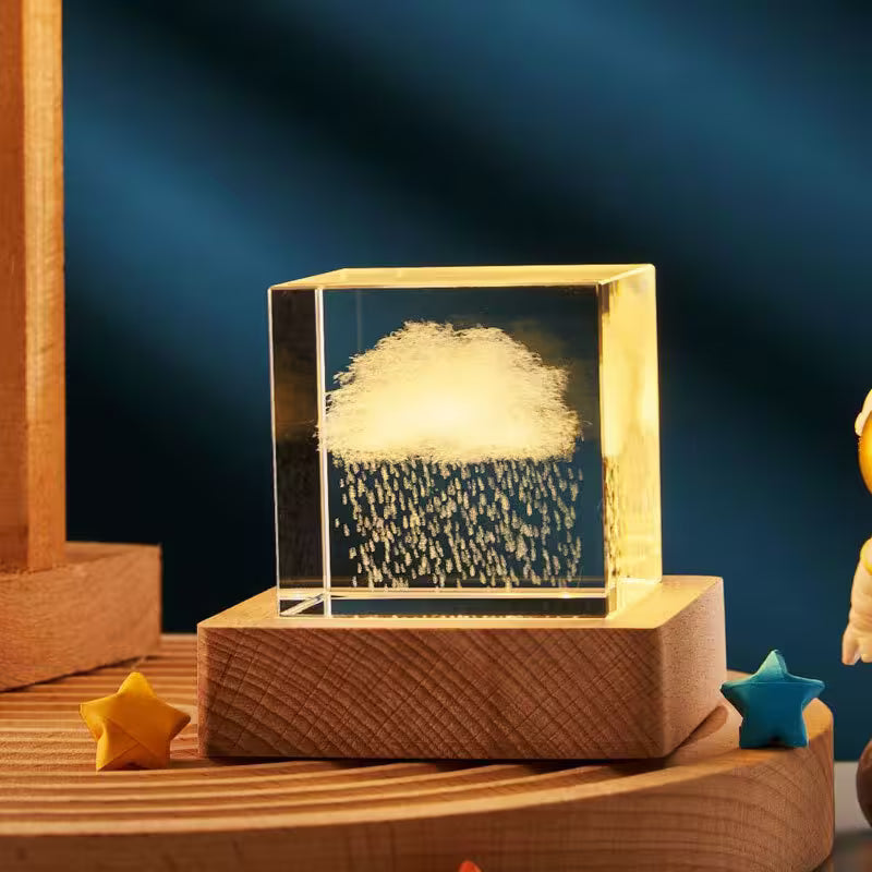 Glass block with cloud and raindrop design on a wooden base against a dark blue background