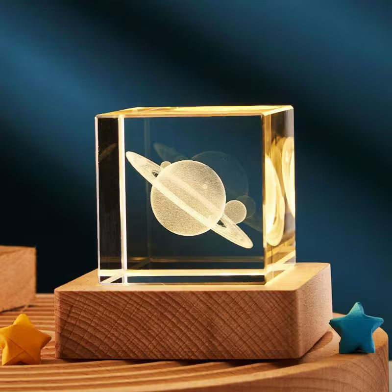 Crystal block with engraved planet design on a wooden base against a dark blue background