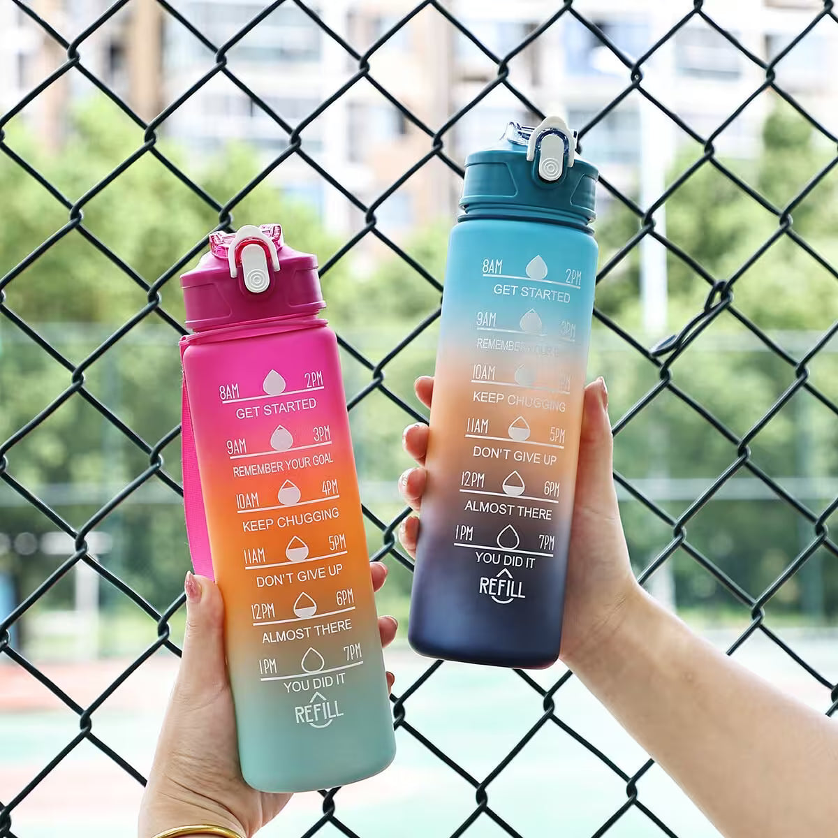 Two colorful water bottles held in front of a chain-link fence.