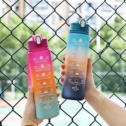 Two colorful water bottles held in front of a chain-link fence.
