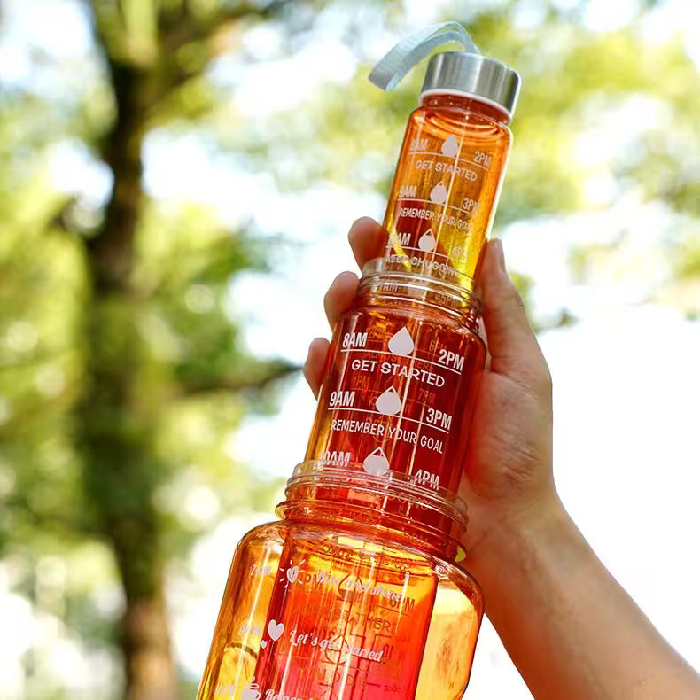 Hand holding an orange motivational water bottle with a blurred green outdoor background