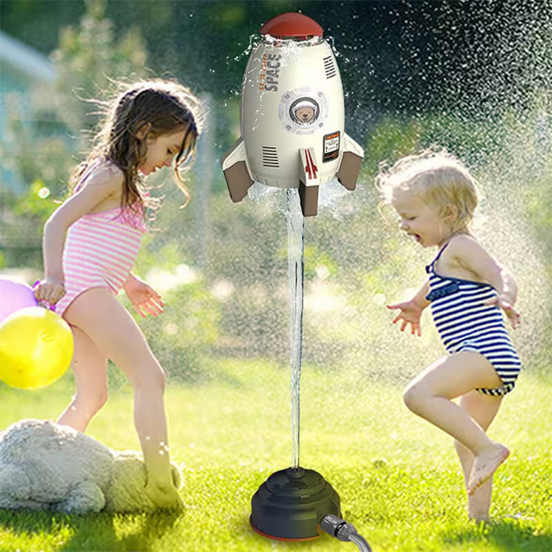 Two children playing with a space-themed sprinkler in a grassy area.