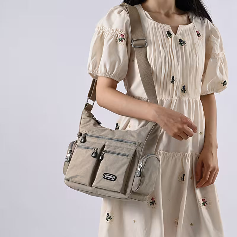 Person wearing a beige dress with floral embroidery holding a beige shoulder bag against a light gray background