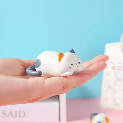 Small white cat figurine held in a hand against a light blue background