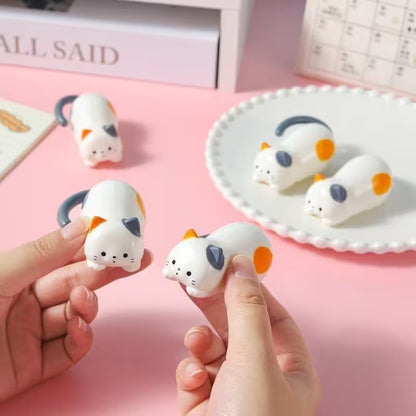Small white animal figurines with orange and gray accents held by a hand on a pink background.